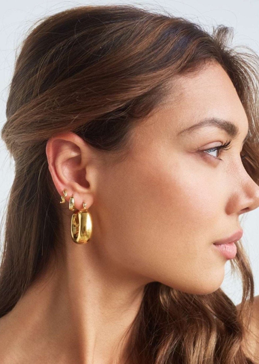 Model wearing large bold square shaped gold hoops 