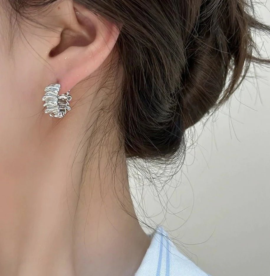 Model wearing silver folded and textured squiggle hoops