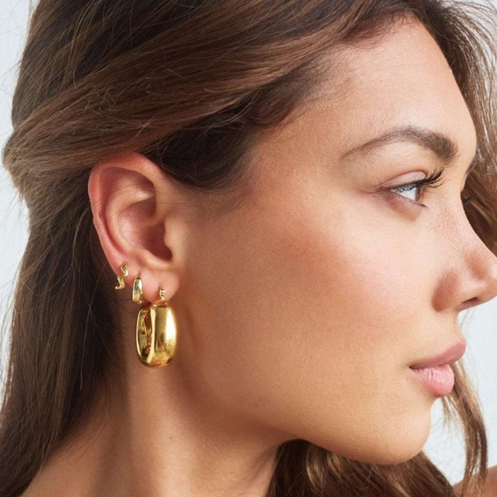 Model wearing large bold square shaped gold hoops 